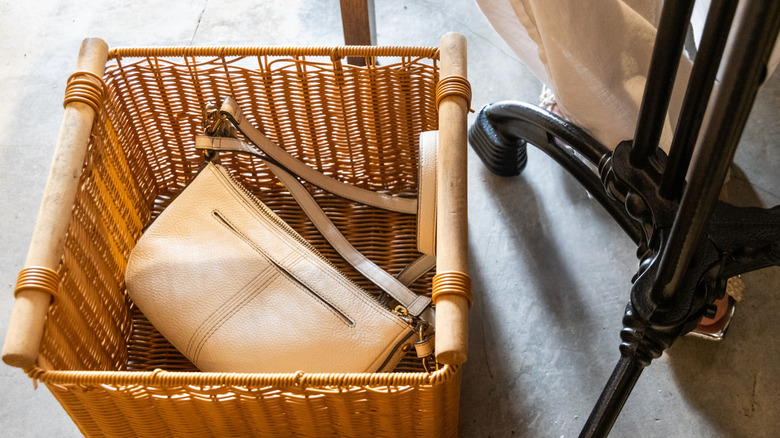A wicker hamper with the lid off and a cream leather handbag inside.
