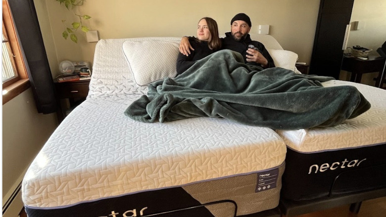 A couple lying under a green throw on the Nectar Premier Adjustable Base in a split king size.