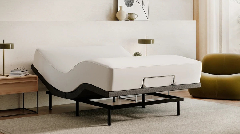 The Nectar Premier Adjustable base with a mattress on it and a bedside table next to it with a lamp on, alongside a modern armchair in the window.