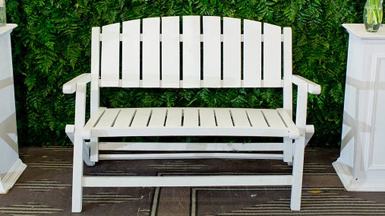 A white glider bench outside against a rich green hedge