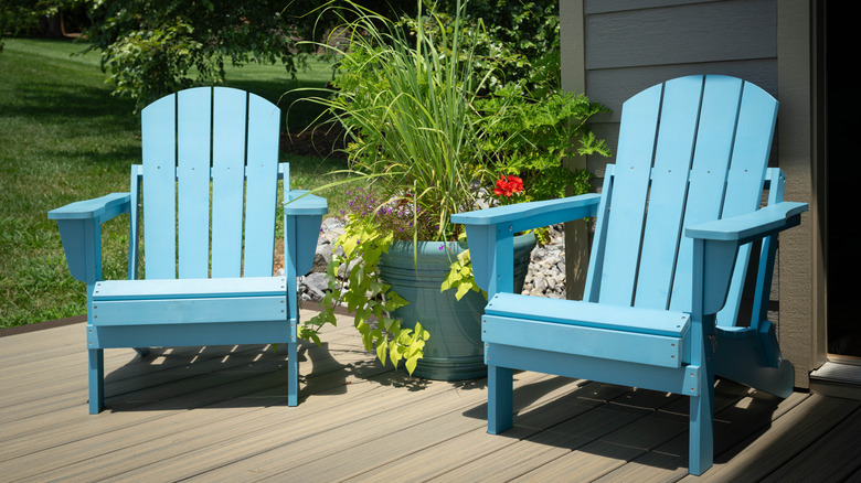 Two light blue Adirondack chairs on a patio with a big potted plant between them