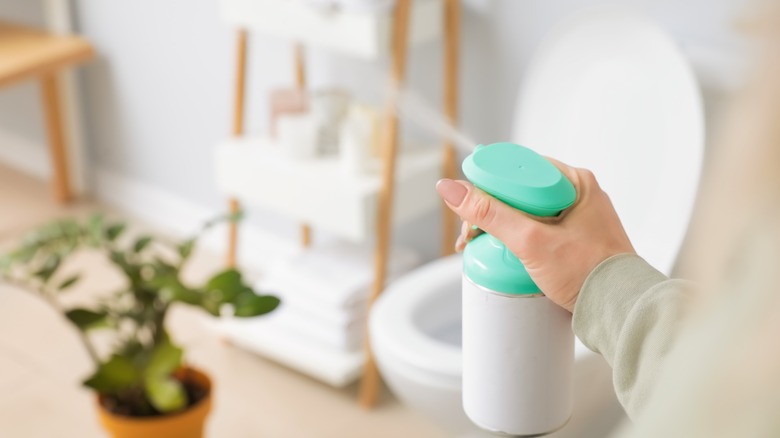 Woman sprays air freshener in bathroom