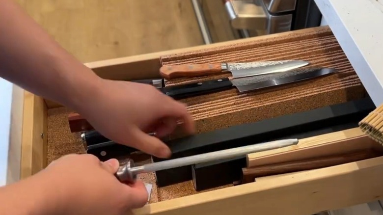 A hand reaching into a drawer with a DIY knife holder made from strips of cork.