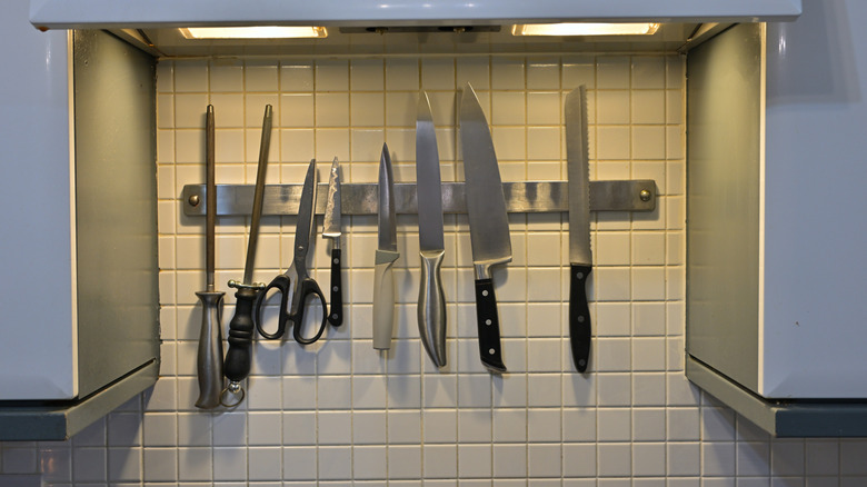 A magnet strip filled with knives on a white tiled kitchen wall.