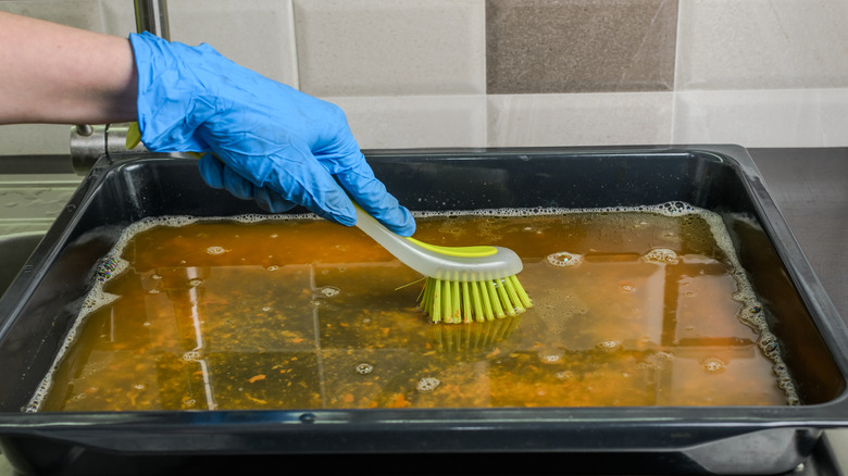 Gloved hand scrubbing baking sheet with bristle brush