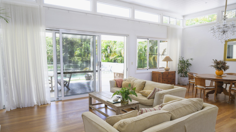The loungeroom of a home with a large sliding glass door and sheer cotton curtains over to the side