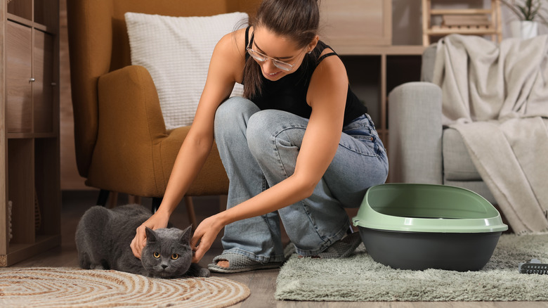 A woman crouched on the ground petting a cat, with a litter box next to her