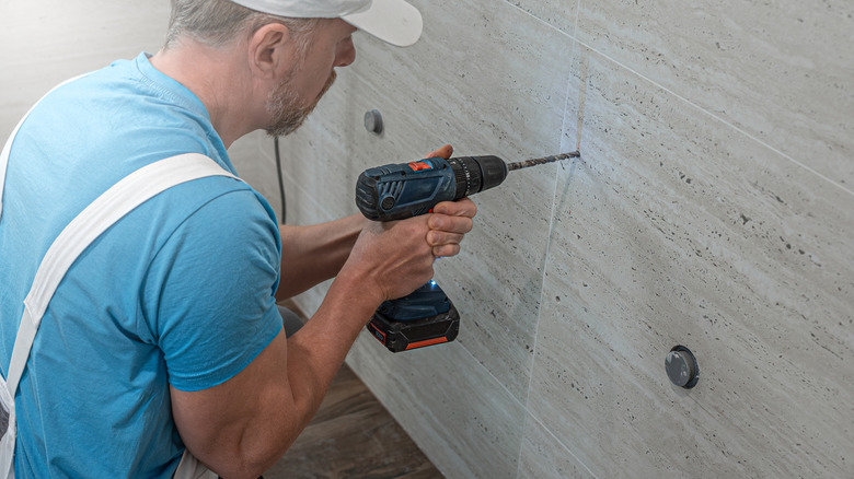 A man drills into a bathroom wall.