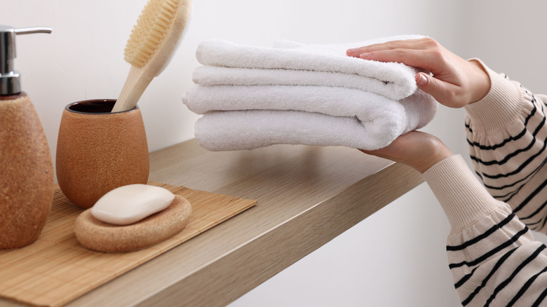 A person puts towels on a floating wooden shelf in a bathroom.