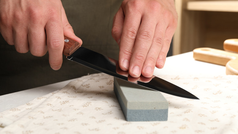 A man sharpening a kitchen knife on a whetstone