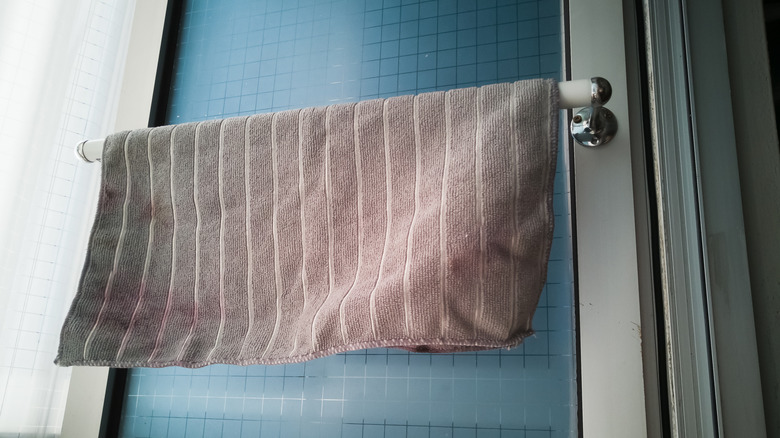 A gray microfiber towel hangs on a railing across a window in a kitchen or bathroom.