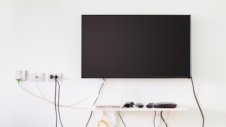 TV mounted on the wall with various wires underneath it and a floating shelf
