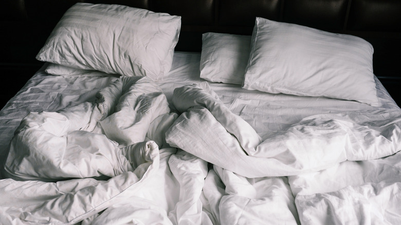 Crumpled white bed sheets with pillows on a bed