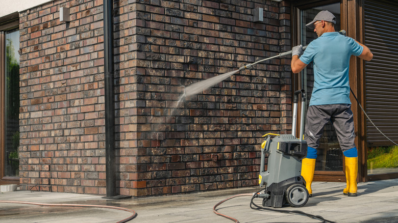 A man pressure washing a home's brick siding