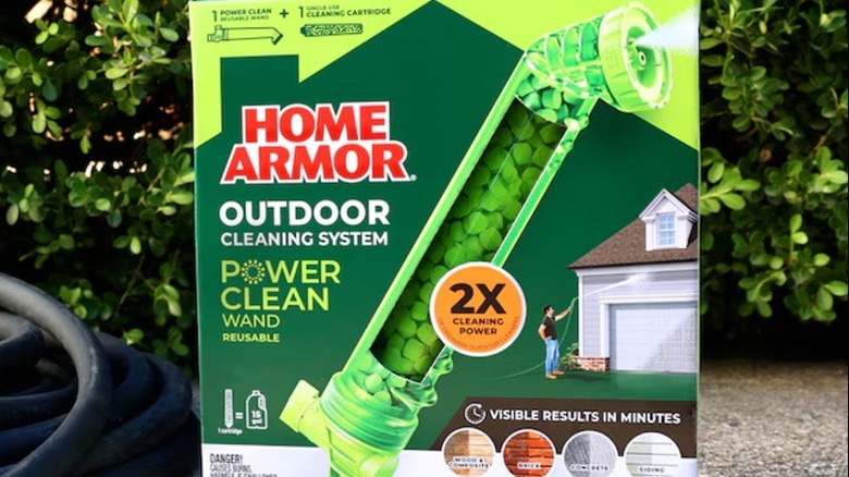 A closeup of the box containing the Home Armor power clean wand with a hose and shrubs in the background