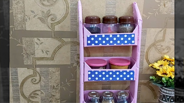 A pink, blue, and white DIY spice rack made from cardboard holds containers of spices