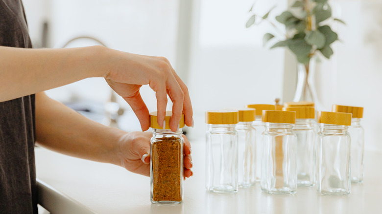 Person's hand closing the lid on a glass jar with red spices. Other empty jars are nearby.