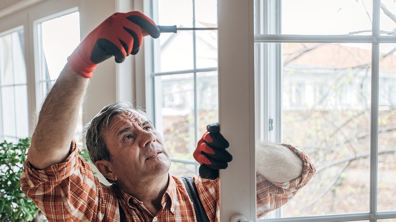An older person looks up at door while using a screwdriver on its frame