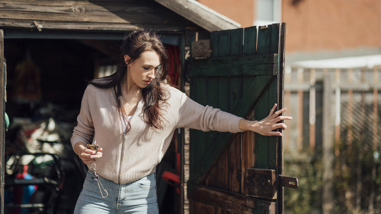 A woman opening an old wooden storage shed