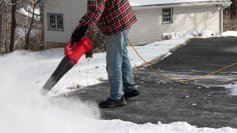 Man using leaf blower to clear snow from driveway
