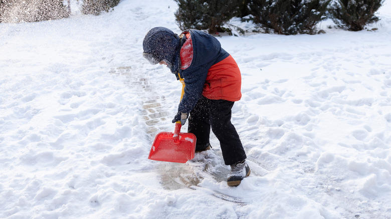 Young boy shoveling snow from walkway