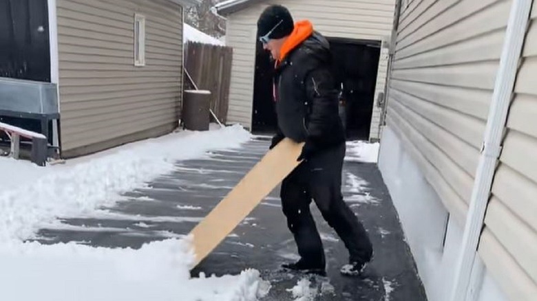 Man moving snow from driveway with a piece of plywood