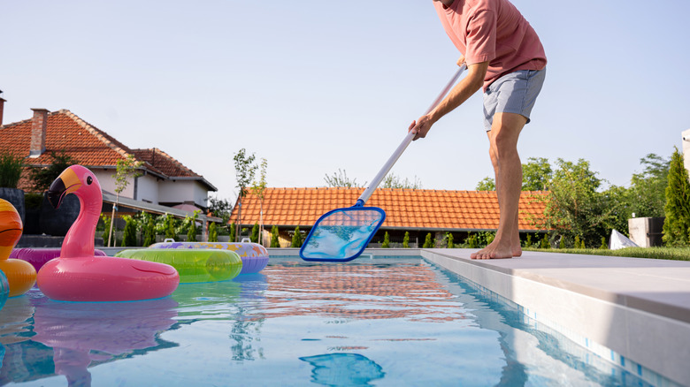 A person cleans a swimming pool with a skimmer