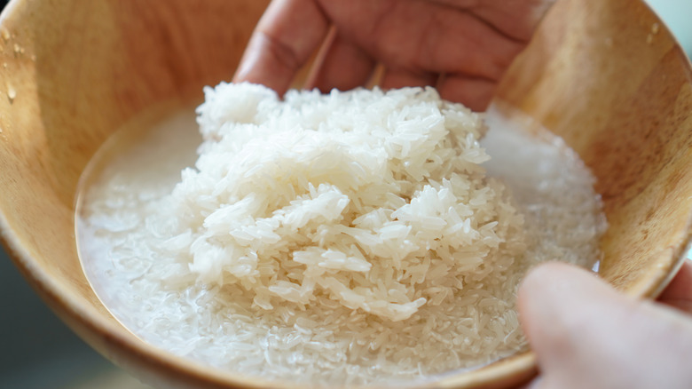Hand stiring rice that is soaking in water in a small wood bowl