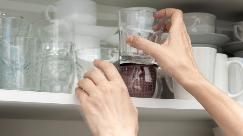 A person grabbing a mug from a full cabinet