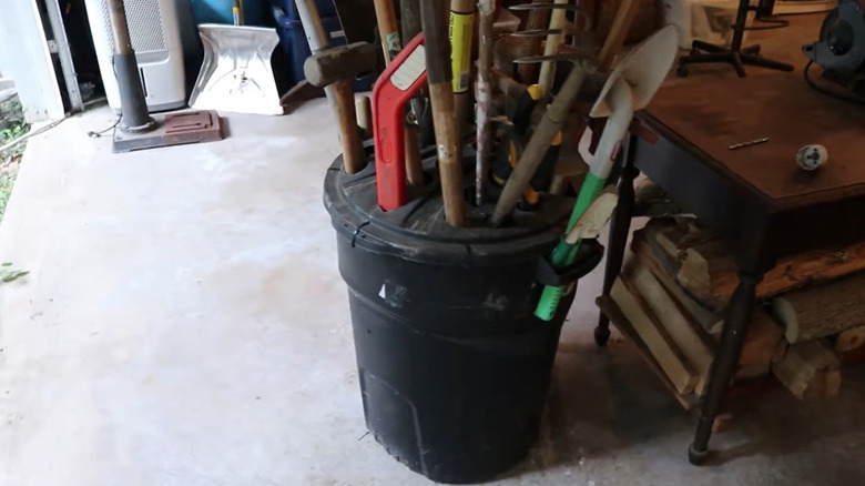 A garbage can provides alternative storage for garden tools