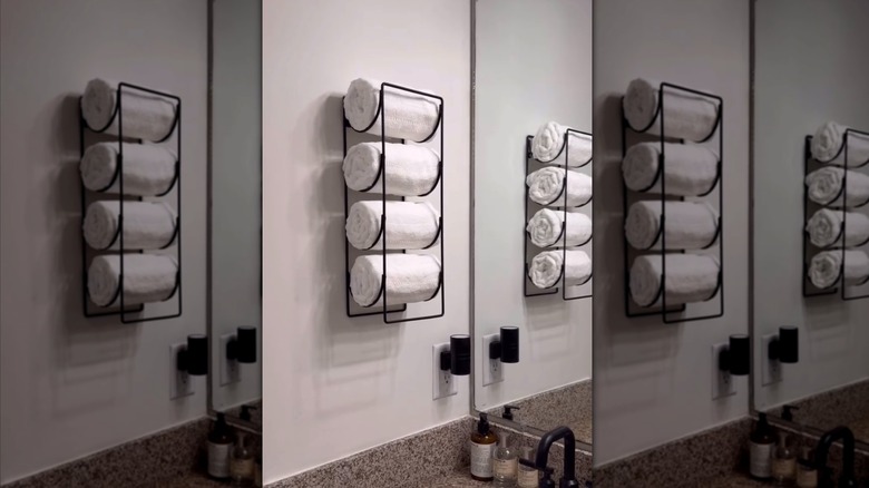 A black metal vertical wine rack installed on a wall and filled with rolled white towels.