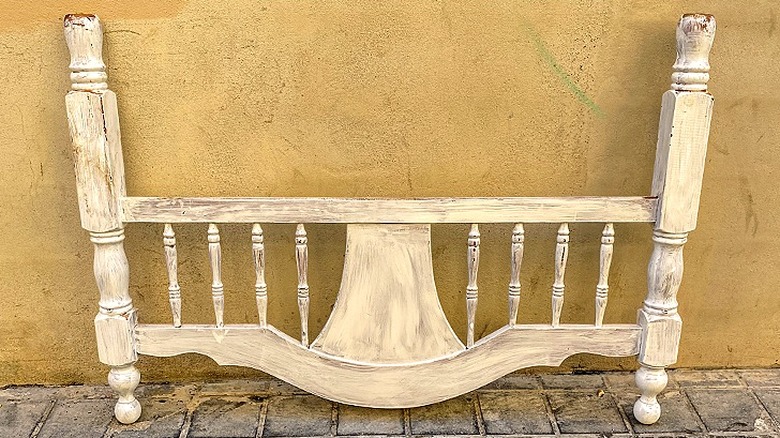 A vintage wooden spindle headboard painted in a cream color rests against a wall.