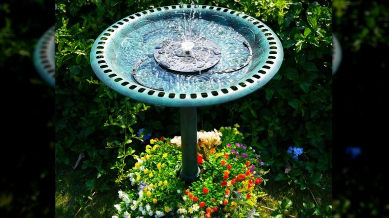 A faux copper-patinaed bird bath with a solar fountain and a planter full of flowers at its base