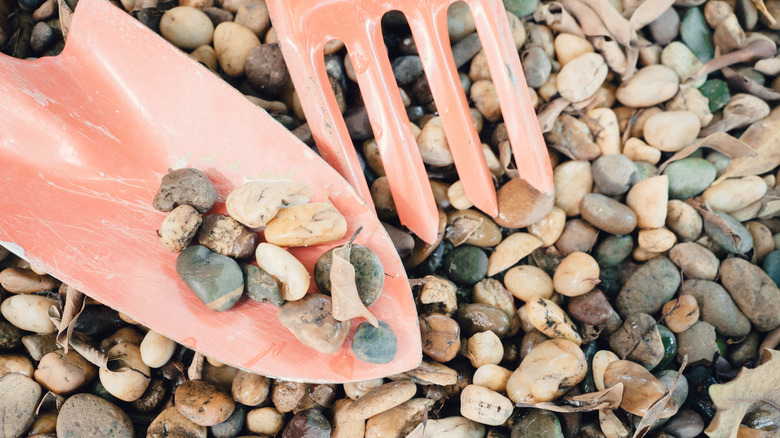 A close-up shot of orange gardening tools above a bed of river rocks