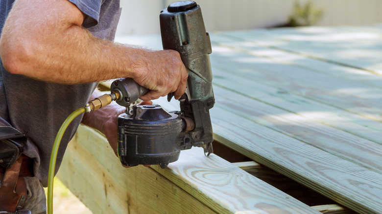 A person using a nail gun to fasten planks on a deck.