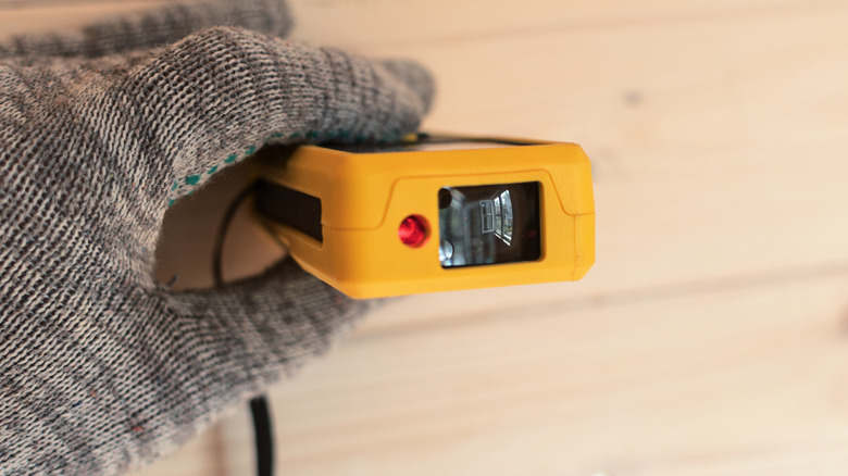 A gloved hand using a laser distance measurer.