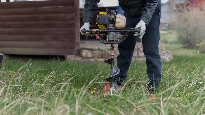 A man using a powered earth auger to dig holes in the ground.