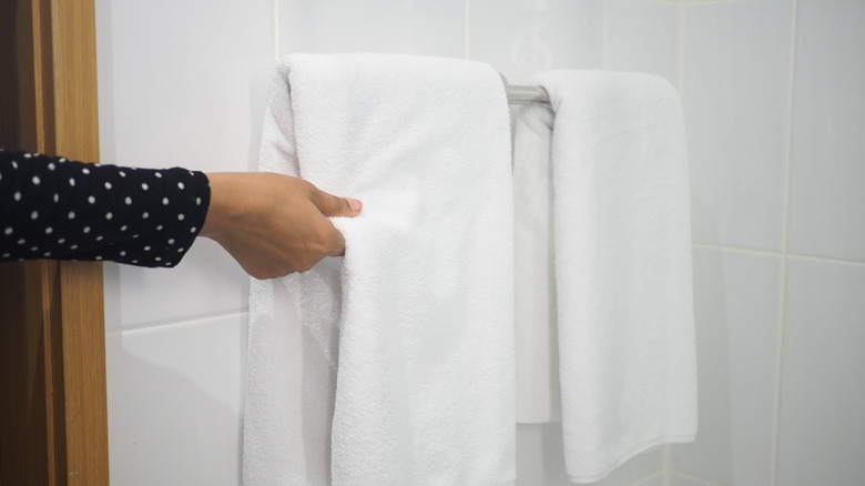 Woman with a white towel on her wet hair, smiling and looking down at towel she's holding. With an empty towel rack on the wall behind her