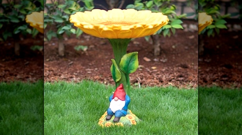 A decorative bird bath in the shape of a sunflower with a gnome relaxing at the bottom