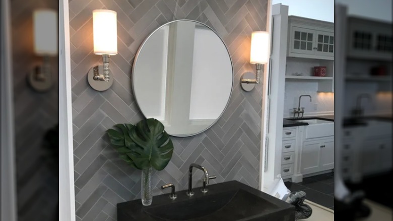 A backsplash behind a sink, mirror and lighting made of ash cement tiles in a herringbone pattern