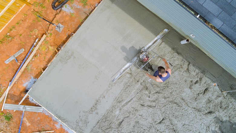 A man uses a tool to smooth poured concrete for a driveway.