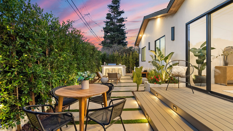 Lush outdoor deck at sunset with tables and chairs, surrounded by greenery.