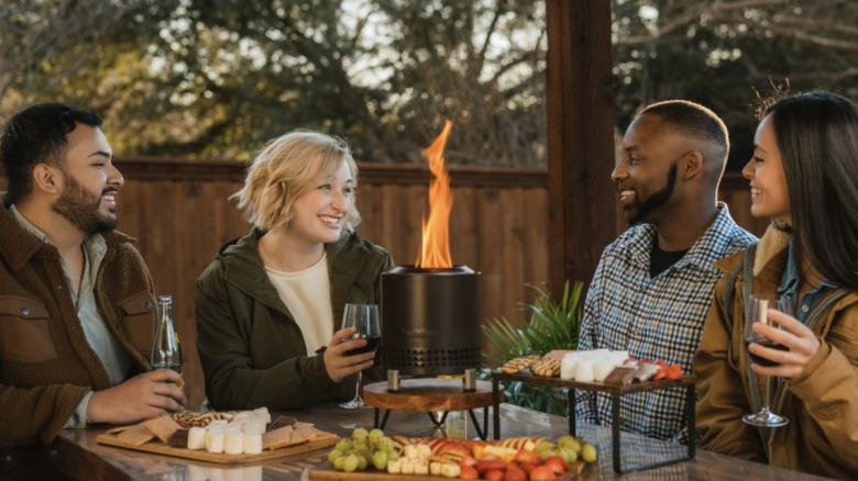 Friends sitting around Mesa XL Solo Stove placed on a table with snacks
