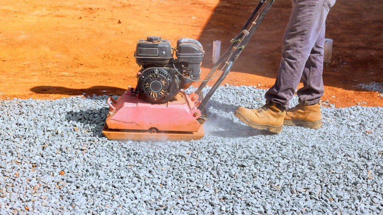 A person using a compactor plate on a crushed stone surface