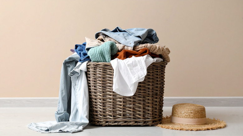 An overflowing wicker laundry basket with a straw hat on the floor next to it.