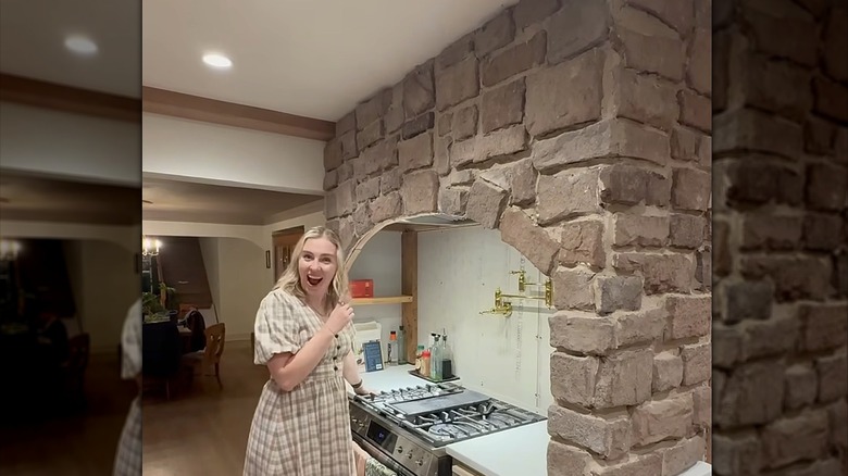 Woman standing in front of a partially assembled stone archway over a range stove with an excited look on her face
