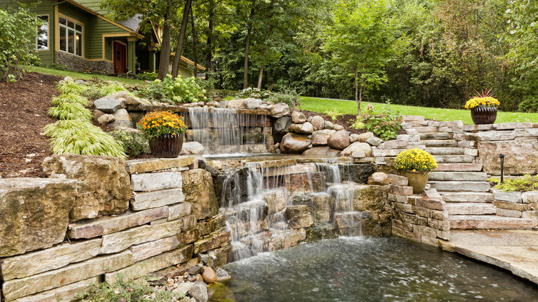 A stone retaining wall with a waterfall that empties into a backyard pond.