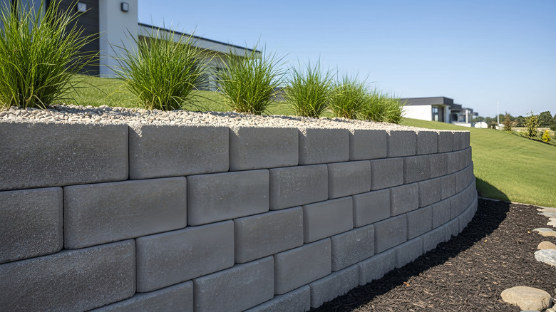 A gray brick retaining wall planted up with ornamental grass and white gravel.