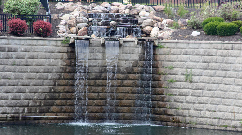 a large retaining wall planted with shrubs and featuring three waterfalls emptying into a pond.