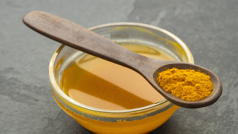 Turmeric in a spoon and some dissolved in water in a bowl